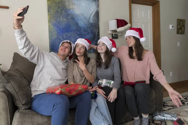 Four college-aged siblings wearing Santa hats pose for selfies.