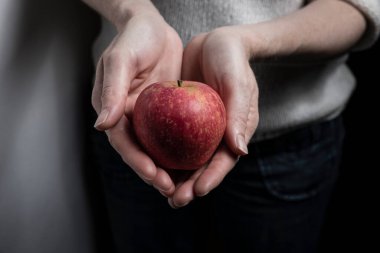 Siyah bir arka planda kırmızı bir elmayı tutan bir elin yakınına.