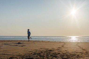 Gün batımında kumsalda yalınayak koşan bir adamın silüeti.