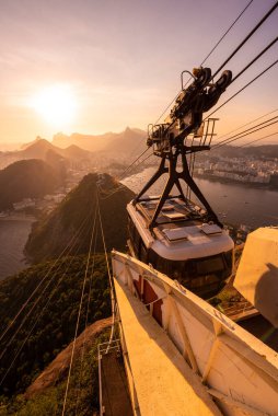 Sugar Loaf dağından Rio de Janeiro, Brezilya 'daki tramvaya, şehre ve okyanusa güzel altın gün batımı manzarası
