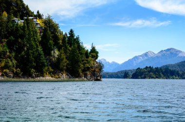 Göl, çam ağaçları ve dağdaki ev. Güneşli yaz günü.