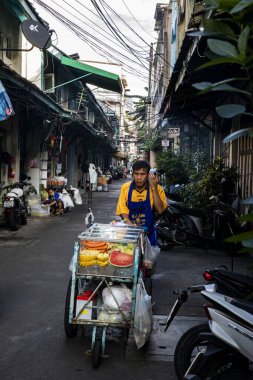 Vendor Pushes Fruit Cart Along Street in Talat Noi Alley in Bangkok