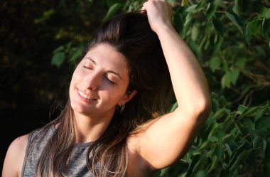 Yeşil bitkilerin arka planında poz veren çekici genç bir kadın.