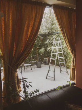 Sarı perdeli bir ev penceresi ve karlı bir günde dışarıda bir merdiven.