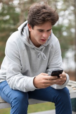 A caucasian male college student looks at his cell phone outdoors