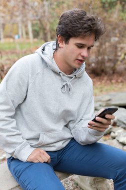A caucasian male college student looks at his cell phone outdoors