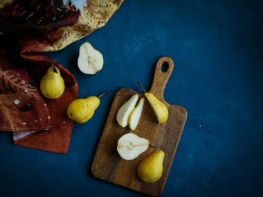 Ahşap kesme tahtasındaki taze sarı armutlar mavi arka planda bulaşık havlusu, düz yatıyordu.