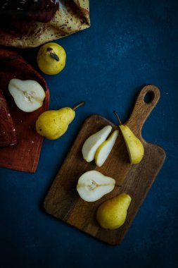 Ahşap kesme tahtasındaki taze sarı armutlar mavi arka planda bulaşık havlusu, düz yatıyordu.