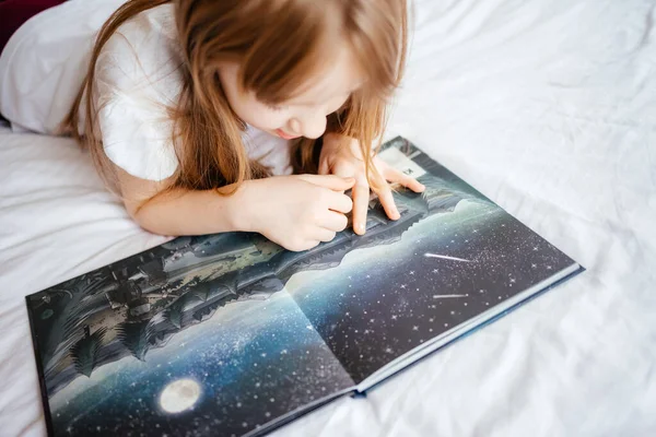 Chica Mira Imágenes Libro Sobre Una Cama Blanca —  Fotos de Stock
