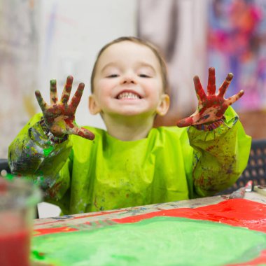 Toddler boy at art class smiling happily and showing his colorful palm