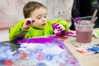 Portrait of a toddler at art classroom holding violet gouache paint