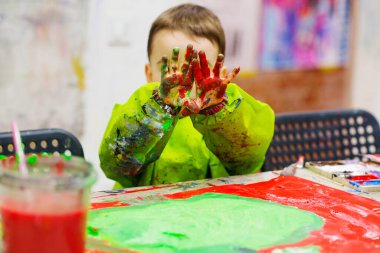 Toddler boy at art class hiding face behind his messy colorful palms