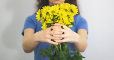Sarı çiçekleri tutan mavi kazaklı esmer kadın.