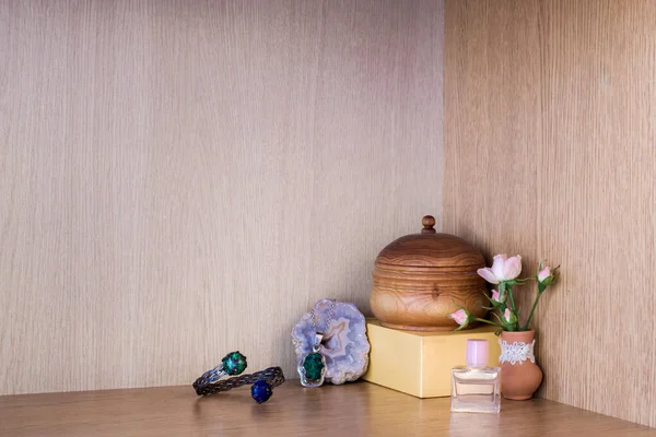 Perfume with jewelry by flower vase in the corner on a wooden shelf