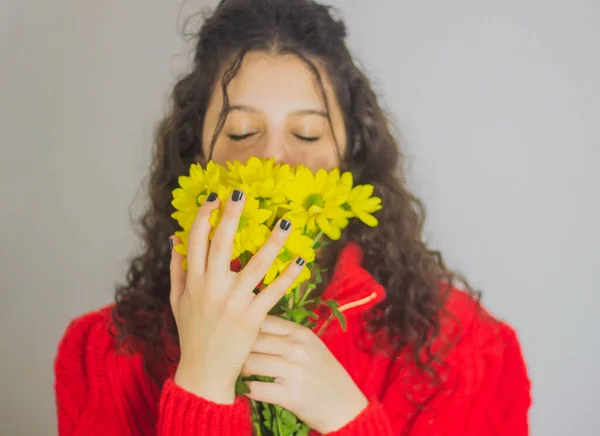 Brunette Woman Curly Hair Red Sweater Smelling Yellow Flowers — Stock Photo, Image