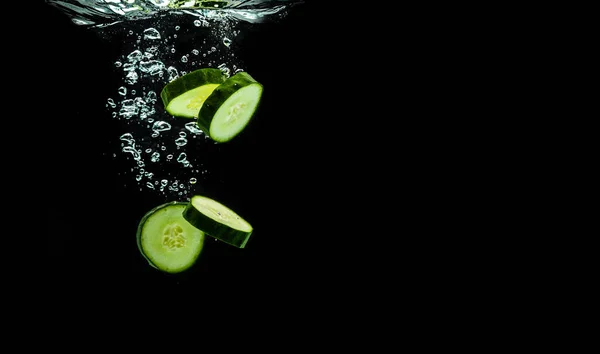 Sliced bio cucumber splashing water isolated on black background. Skin moisturizing cosmetics concept