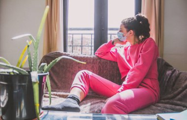 Kanepede koruyucu maskeli, üzgün genç bir kadın, kovid19 konsepti