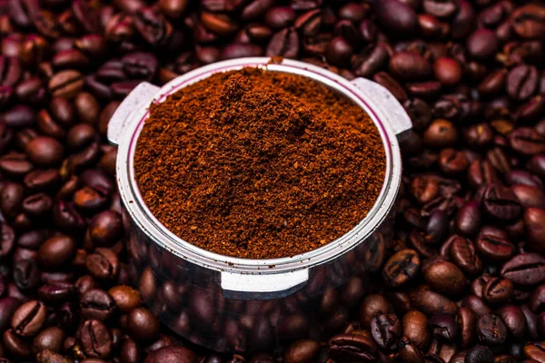 Background with ground coffee in portafilter surrounded by roasted coffee beans,