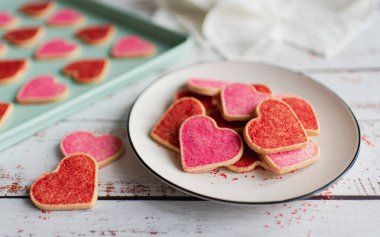 Beyaz ahşap arka planda kırmızı ve pembe kalp şeklinde kurabiyeler..