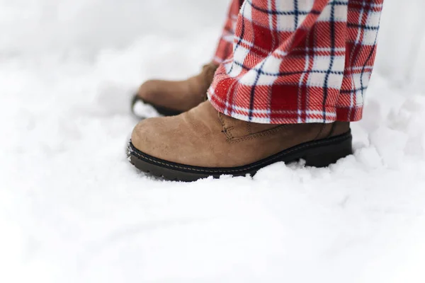 Legs of anonymous woman with winter boots standing on white snow