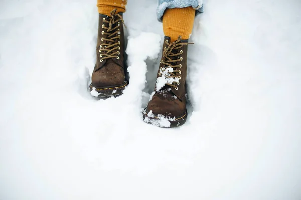 Legs of anonymous woman with winter boots standing on white snow