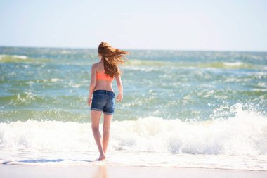 Okyanusun kıyısında mayolu genç kızıl saçlı kız..
