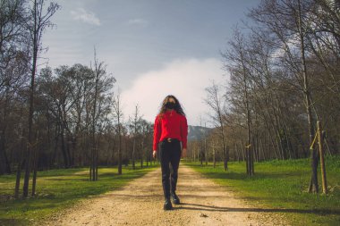 Yüzü maskeli genç bir kadın ormanın yakınındaki kirli yolda yürüyor.