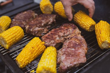 Biftek ve mısır koçanları ızgarada kızartılıyor.