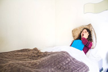 Genç kadın yatakta uzanıp kitap okuyor.