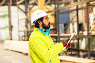 Depoda çalışan kasklı ve sakallı bir işçi.