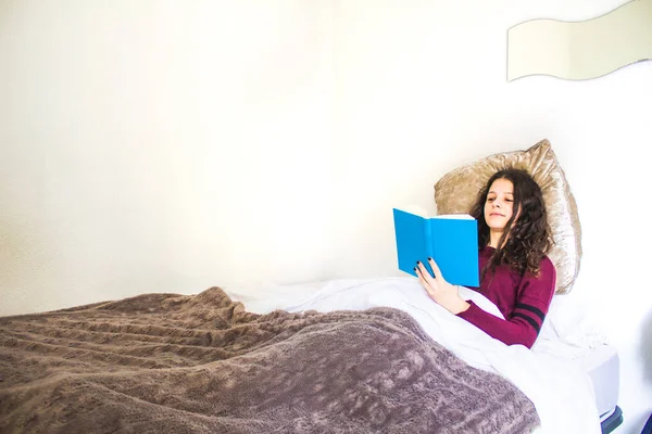 Genç kadın yatakta uzanıp kitap okuyor.