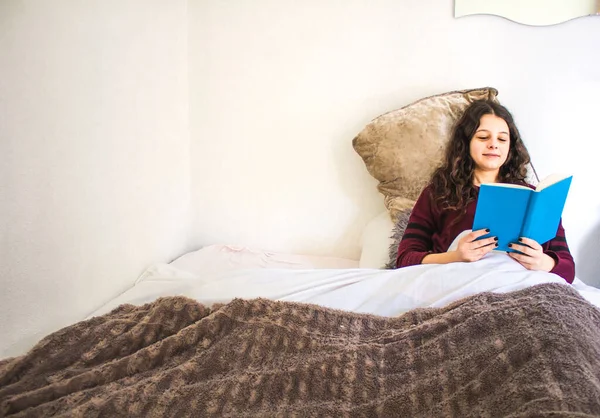 Genç kadın yatakta uzanıp kitap okuyor.