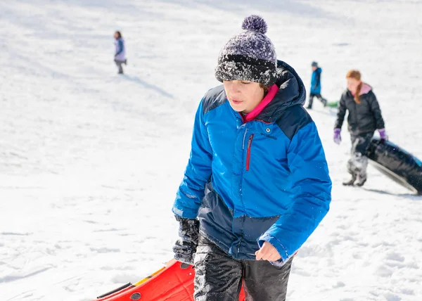 Çocuk turuncu kızağıyla kızak tepesinde yürüyor..