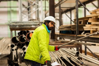 Depoda çalışan kasklı ve sakallı bir işçi.