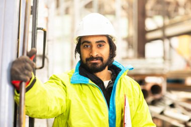 Depoda çalışan kasklı ve sakallı bir işçi.