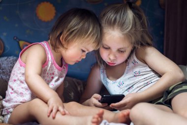 Kız kardeşler yataklarında akıllı telefonlara bakıyor. teknolojik kavram
