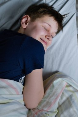 Yatağında, battaniyesinin altında gülümseyen çocuk.