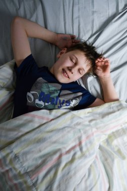 Yatağında, battaniyesinin altında gülümseyen çocuk.