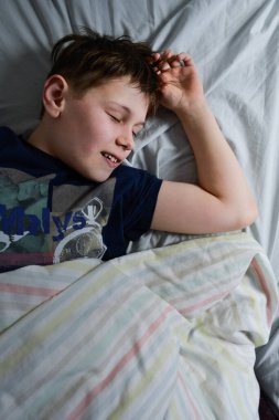 Yatağında, battaniyesinin altında gülümseyen çocuk.