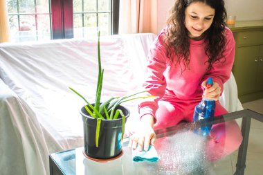 Evi paçavra ve spreyle temizleyen genç bir kadın.