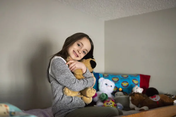 Little girl on top of a bunk bed hugging a stuffed animal.