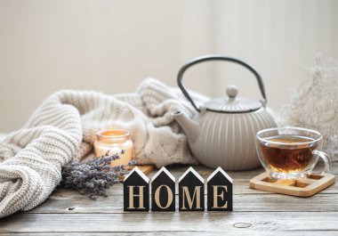 Çaydanlık ve ahşap bir yüzey üzerinde çay ile sakin bir hayat örgü ögesi, samimi detaylar ve bulanık bir arka planda dekoratif bir kelime olan ev..