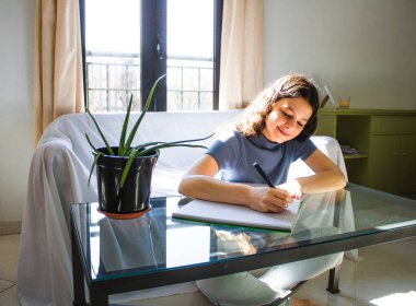 Genç bayan oturma odasında çalışıyor ve yazıyor.