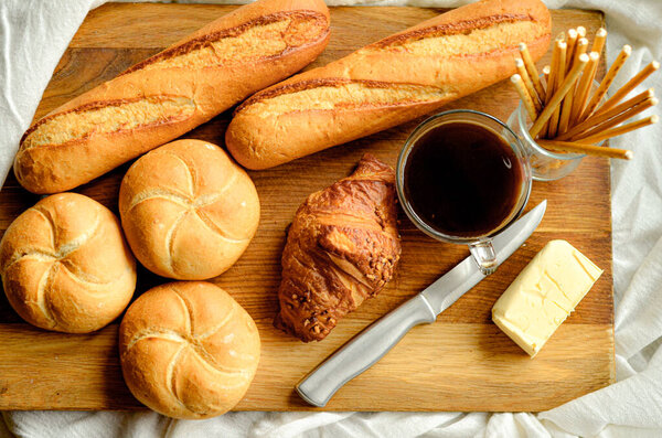 breakfast on a white tablecloth, coffee, rolls, butter, knife, wooden