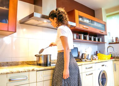 Genç bir kadın mutfakta yemek pişiriyor.