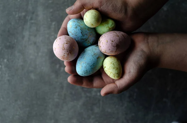 Easter colored eggs in hands on a gray background, top view