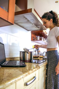 Genç bir kadın mutfakta yemek pişiriyor.