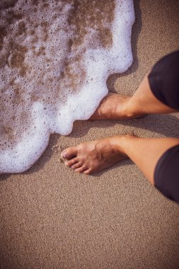 Hawaii 'de güneşli bir günde deniz köpüğü bir kadının ayaklarını hafifçe yıkıyor.