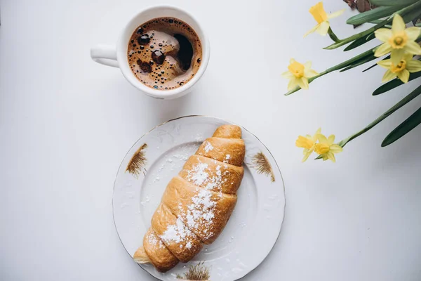 croissant on a plate, a cup of coffee and flowers