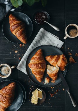 Kahve ve reçelli kruvasan tabakları yukarıdan siyah masaya..